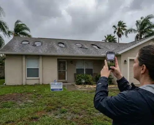 A Tampa homeowner documenting exterior roof damage and missing shingles with a smartphone to support a homeowners insurance claim after a severe Florida storm.