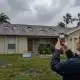 A Tampa homeowner documenting exterior roof damage and missing shingles with a smartphone to support a homeowners insurance claim after a severe Florida storm.